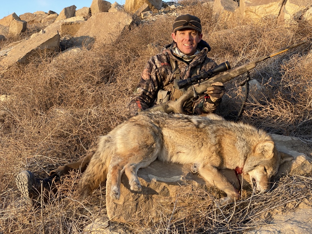 a man in camouflage with a gun and a dog lying on the ground